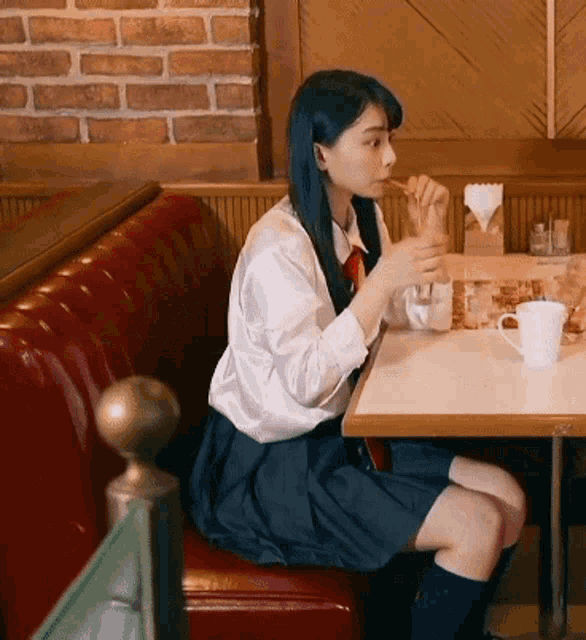 a girl in a school uniform sits at a table in a diner