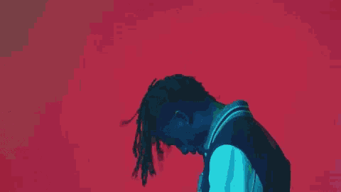a man with dreadlocks is standing in front of a red wall .