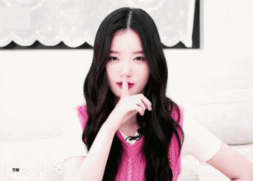 a woman in a pink vest is holding her finger to her mouth