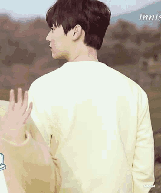 a man in a white sweater is standing in a field with his hand outstretched .
