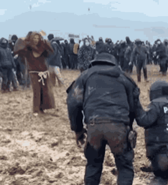a group of people are gathered in a muddy field with a police officer in the foreground