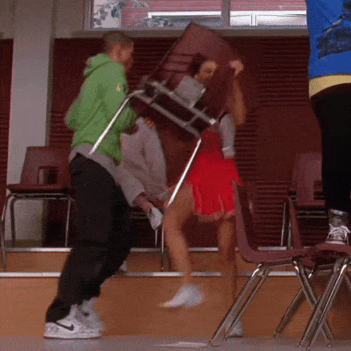 a man in a green hoodie holds a chair over a cheerleader 's head