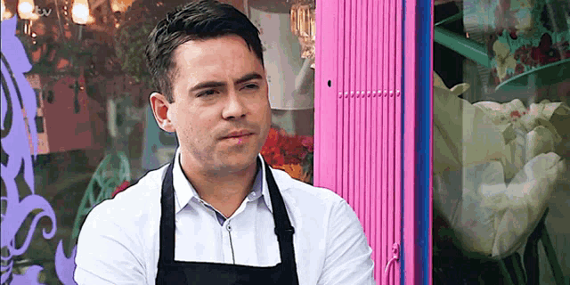 a man in an apron is standing in front of a pink wall