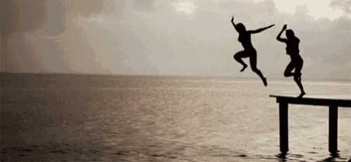two women are jumping into the ocean from a dock .