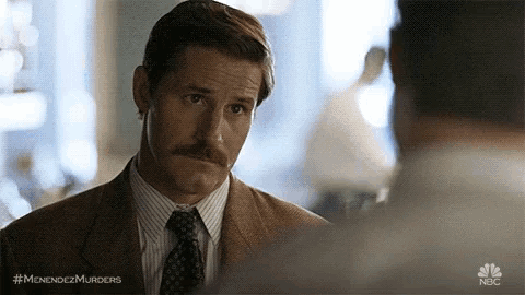 a man in a suit and tie is talking to another man in a room .