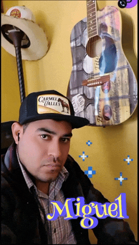 a man wearing a hat that says carmel valley is standing in front of a guitar