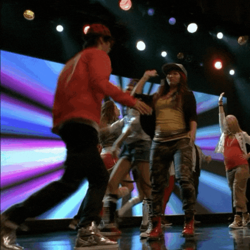 a group of people are dancing on a stage and one of them is wearing a yellow shirt that says nike