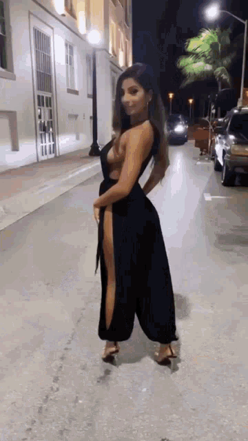 a woman in a black dress is walking down a street at night .