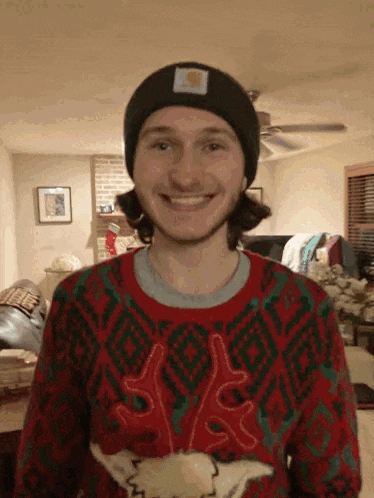 a man wearing a christmas sweater and a beanie is smiling