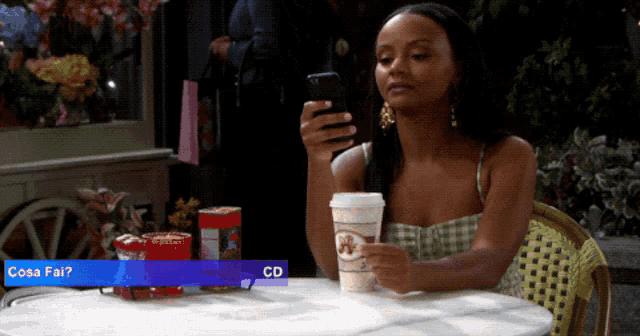 a woman sitting at a table with a cup of coffee looking at her phone with a cd displayed below her