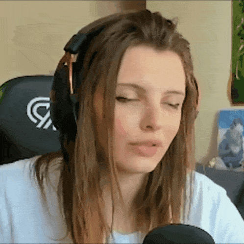 a woman wearing headphones and a white shirt is sitting in front of a microphone with her eyes closed .