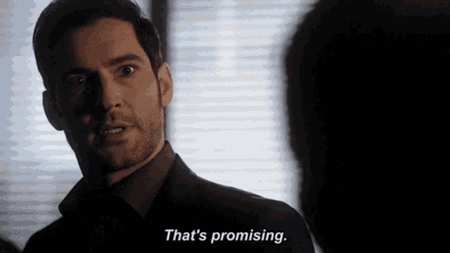a man in a suit says that 's promising in a dark room