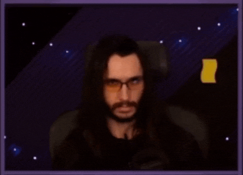 a man with long hair and glasses is sitting in front of a microphone in a dark room .
