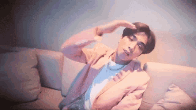 a young man in a pink suit is sitting on a couch with his hands on his head .