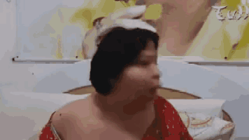 a woman with a bandage on her head is sitting on a bed in front of a picture .