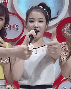 a woman singing into a microphone while giving a thumbs up