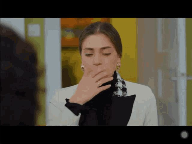 a woman covering her mouth with her hand while wearing a white jacket
