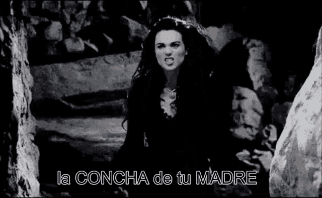 a woman in a black dress is standing in a cave with the words la concha de tu madre above her .