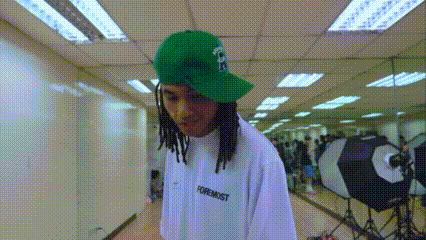 a man with dreadlocks wearing a green hat and a white shirt that says turmmist