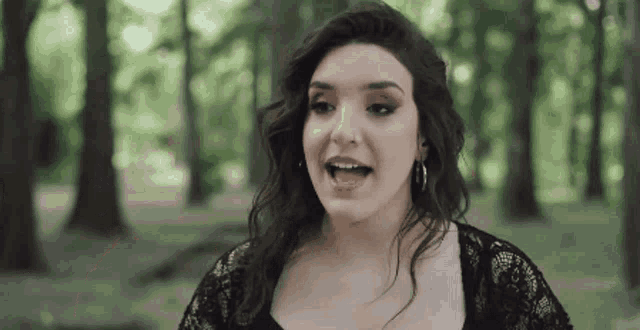 a woman in a black dress is standing in the woods and singing .