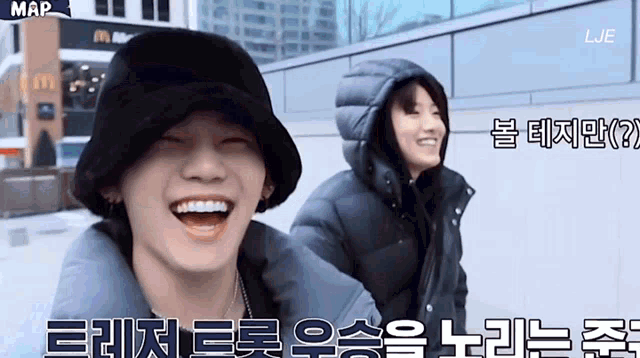 a man wearing a black hat is laughing next to another man wearing a black jacket with a hood .
