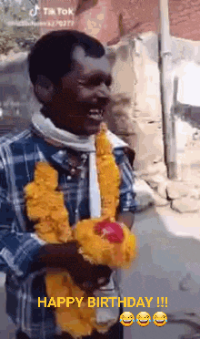 a man wearing a garland of yellow flowers is holding a bouquet of flowers and smiling .
