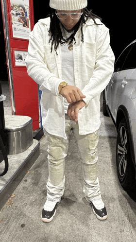 a man wearing a white shirt and a beanie stands in front of a silver car