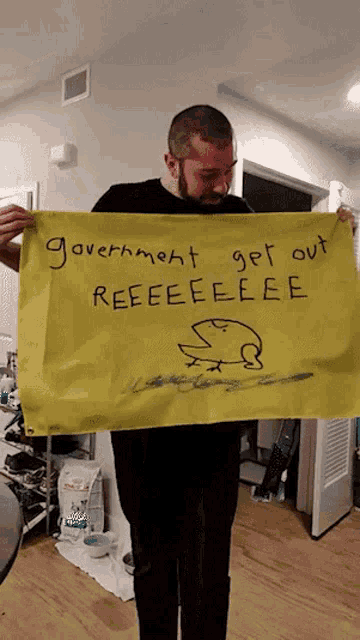 a man holds up a yellow sign that says government get out reeeeeeeee