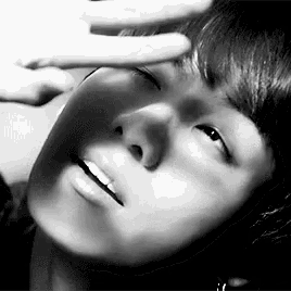 a close up of a person 's face with their hand on their forehead in a black and white photo .