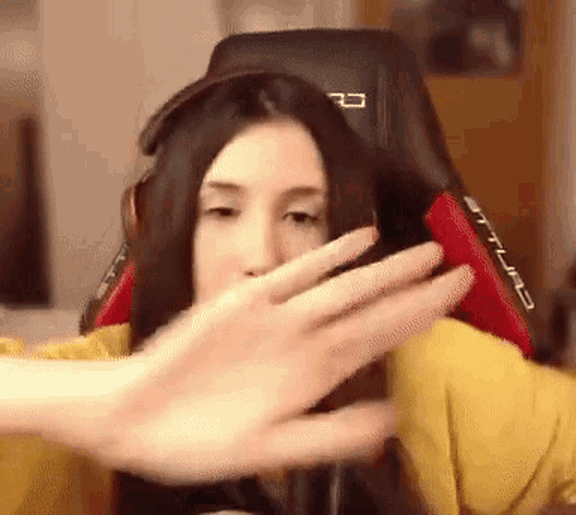 a woman is sitting in a gaming chair and covering her face with her hands .