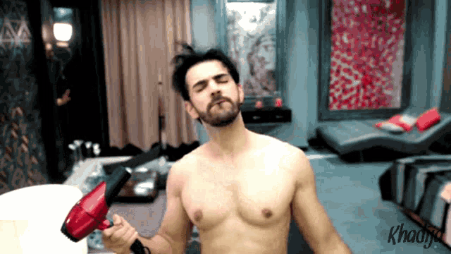 a shirtless man is holding a red hair dryer in a room that says ' khadiy ' on the bottom