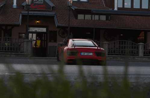 a red sports car is parked in front of a restaurant called budweiser