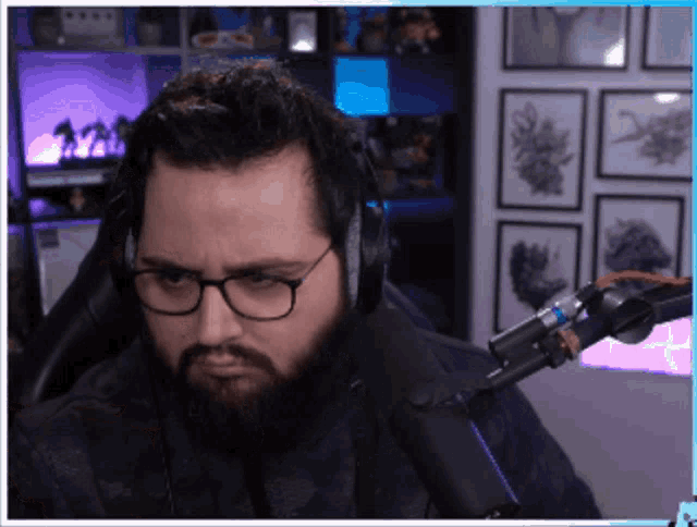 a man with a beard wearing glasses and headphones is sitting in front of a microphone