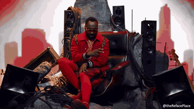 a man in a red jacket sits in a chair in front of speakers