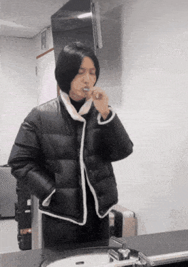 a person in a black jacket brushing their teeth in front of a sink