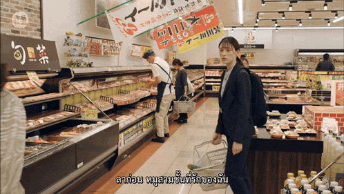 a woman in a suit carrying a basket walks through a grocery store aisle