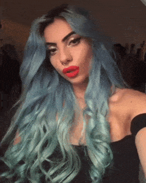 a woman with blue hair and red lips is taking a selfie .