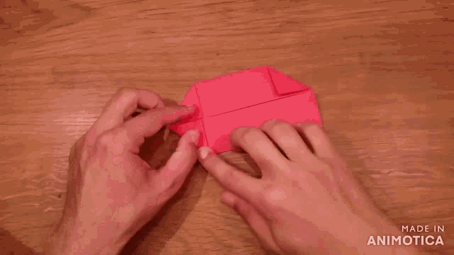 a person is holding a piece of red paper on a wooden table ..