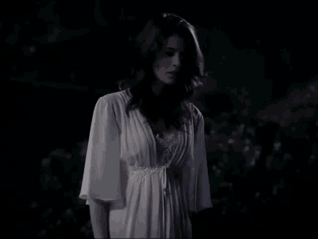 a woman in a white dress is standing in a dark forest