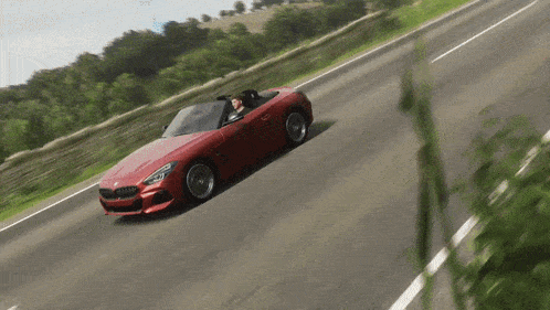 a red sports car is driving down a road with trees in the background