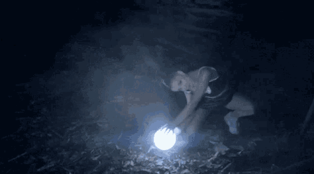 a woman is kneeling down in the dark holding a light bulb