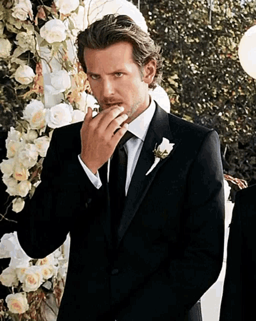 a man in a black suit and tie covering his mouth