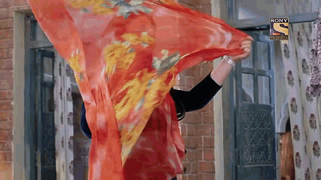 a woman is holding a scarf in front of a brick building .