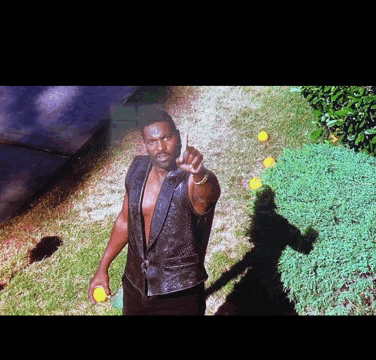 a man in a black vest is pointing at something in the grass