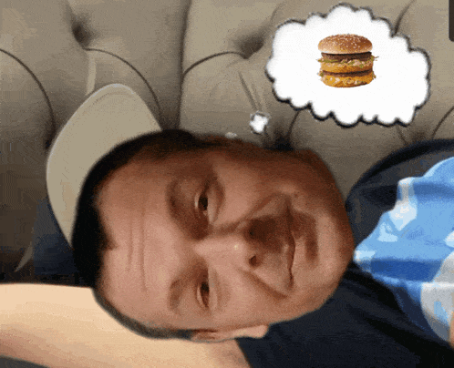 a man is laying on a couch with a thought bubble of a hamburger above his head