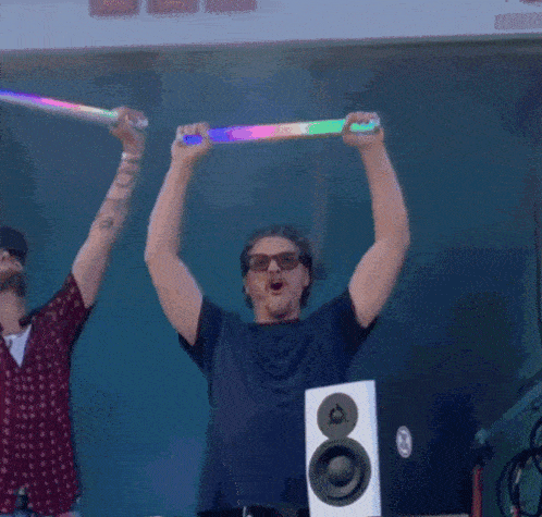 a man wearing sunglasses is holding up a rainbow light stick