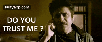 a man with a mustache is talking on a cell phone with the words `` do you trust me '' written on the bottom .