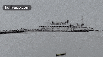 a black and white photo of a large ship in the ocean with a boat in the foreground .