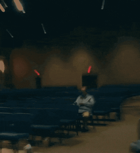 a man sits in an auditorium with a red exit sign