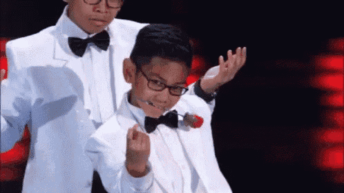 two young boys in tuxedos and bow ties are dancing on stage .